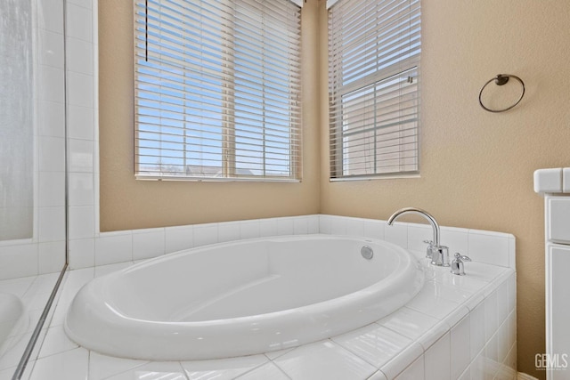 full bathroom with a bath, a textured wall, and a healthy amount of sunlight