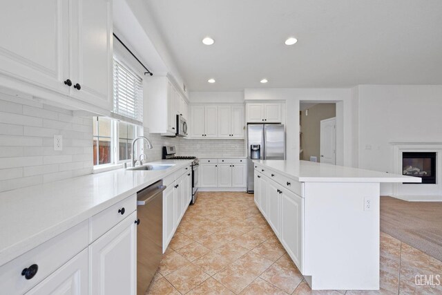 kitchen featuring stainless steel appliances, a sink, tasteful backsplash, white cabinetry, and a kitchen island