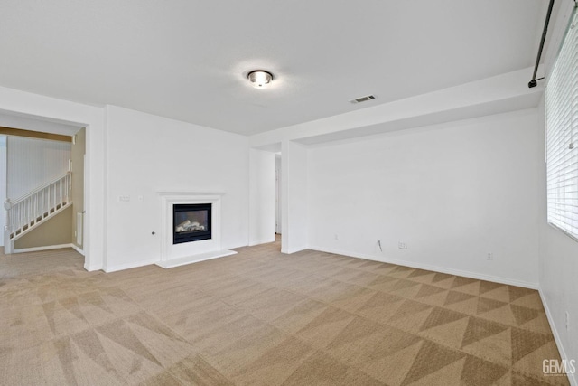 unfurnished living room featuring a glass covered fireplace, visible vents, stairs, and light colored carpet