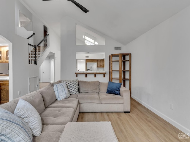 living area featuring high vaulted ceiling, visible vents, baseboards, stairway, and light wood-type flooring