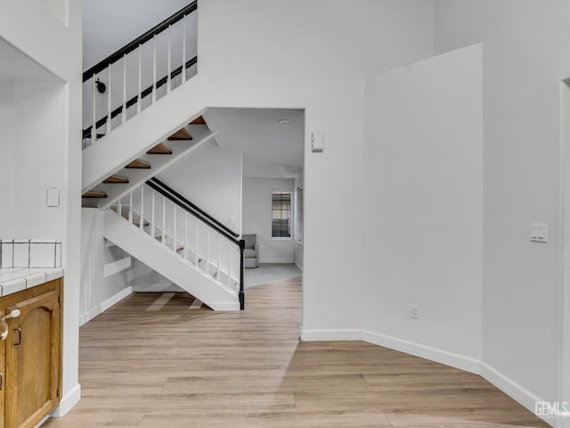 stairway featuring a towering ceiling, baseboards, and wood finished floors