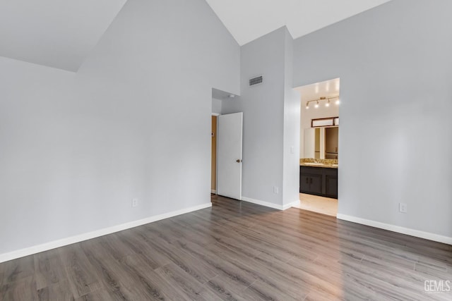 unfurnished bedroom with high vaulted ceiling, visible vents, baseboards, light wood finished floors, and ensuite bath