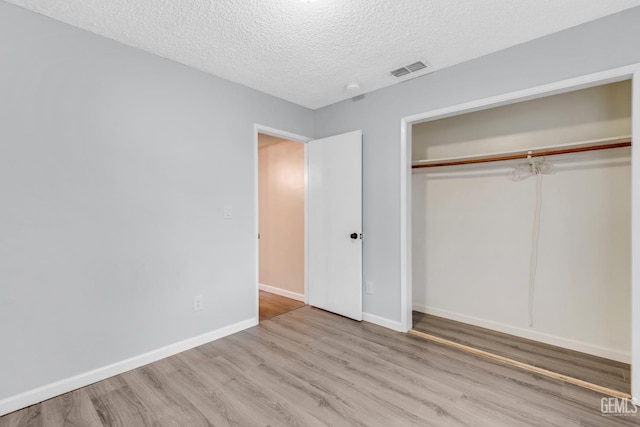 unfurnished bedroom with a textured ceiling, light wood-style flooring, visible vents, baseboards, and a closet