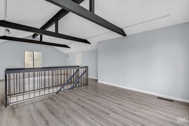 spare room featuring lofted ceiling with beams, light wood finished floors, baseboards, and visible vents