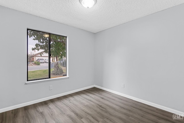 unfurnished room with a textured ceiling, wood finished floors, and baseboards