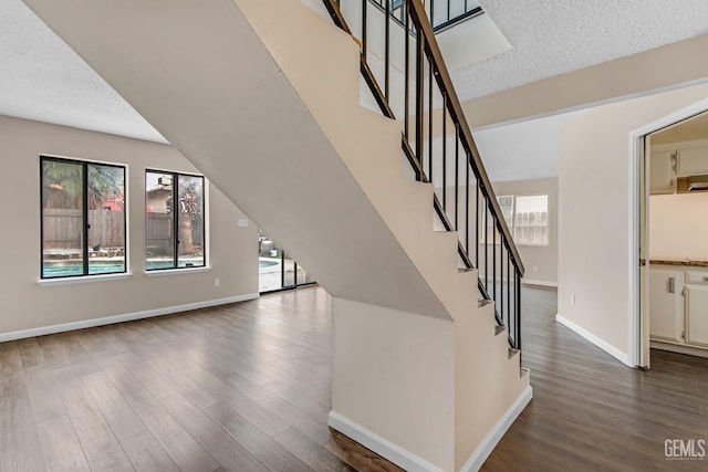 stairway featuring a textured ceiling, wood finished floors, lofted ceiling, and baseboards