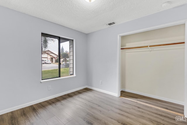 unfurnished bedroom featuring a textured ceiling, wood finished floors, visible vents, baseboards, and a closet