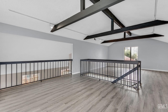 empty room with baseboards, vaulted ceiling with beams, and light wood finished floors