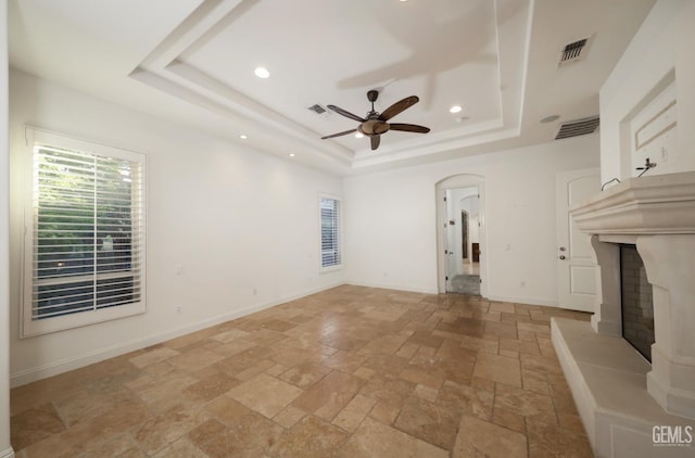 12603 Clay Creek Ct, Bakersfield, CA 93312 - unfurnished living room featuring stone tile flooring, a ceiling fan, a raised ceiling, a high end fireplace, and arched walkways