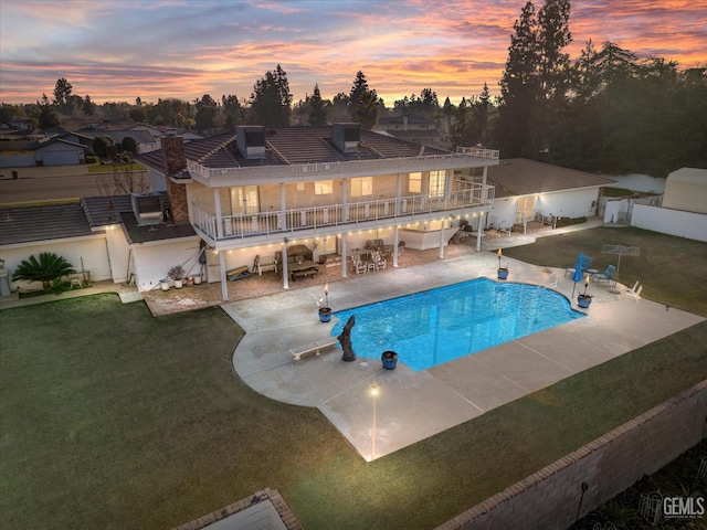 pool at dusk featuring a lawn and a patio