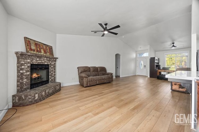 living room featuring arched walkways, vaulted ceiling, a brick fireplace, and light wood-style flooring