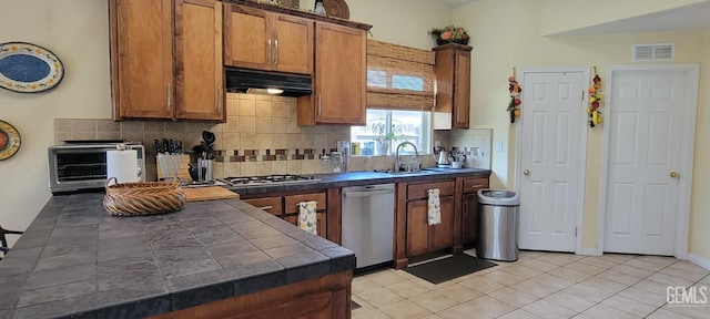 5308 Benevento Ct, Bakersfield, CA 93308 - kitchen with brown cabinetry, tile countertops, gas stovetop, dishwasher, and under cabinet range hood