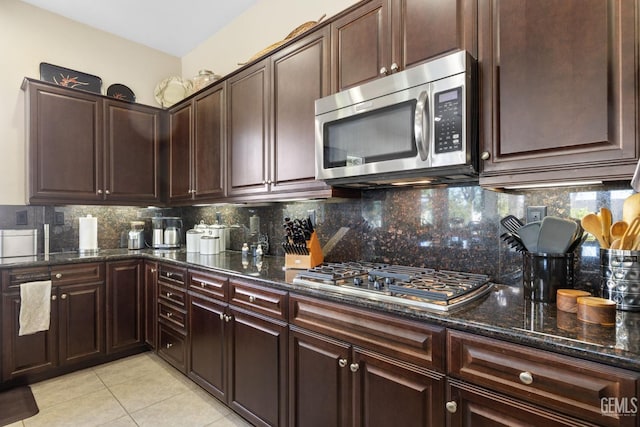 kitchen featuring tasteful backsplash, stainless steel appliances, dark stone counters, light tile patterned floors, and dark brown cabinets