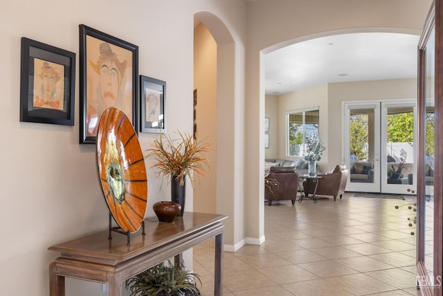 hallway with arched walkways, light tile patterned floors, french doors, and baseboards