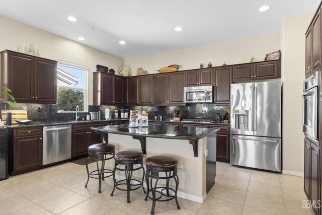 kitchen featuring decorative backsplash, dark brown cabinetry, appliances with stainless steel finishes, a kitchen bar, and a center island