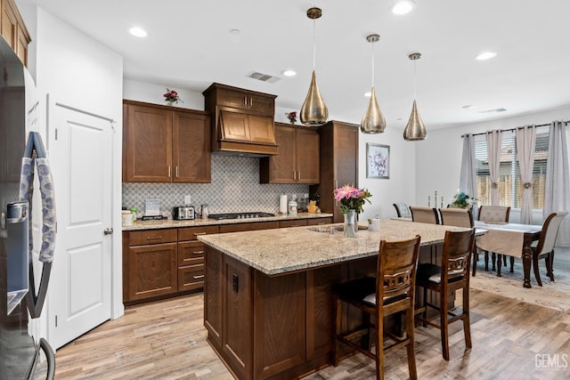 7900 Linden Tree Ave, Bakersfield, CA 93313 - kitchen featuring custom exhaust hood, stainless steel gas stovetop, decorative backsplash, light wood finished floors, and visible vents
