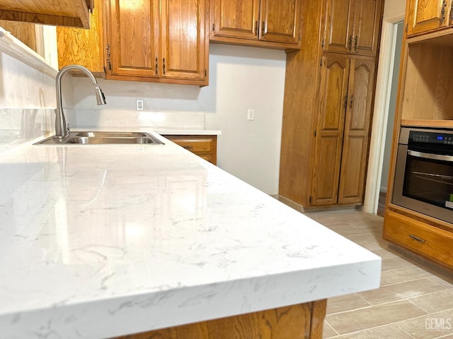 615 Cypress St, Bakersfield, CA 93304 - kitchen with stainless steel oven, a sink, brown cabinetry, and light stone countertops