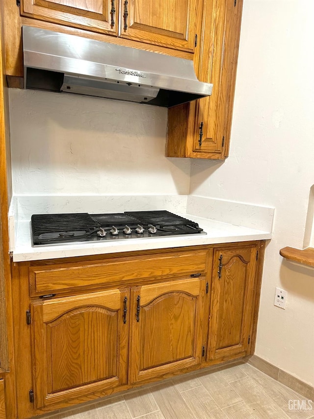 615 Cypress St, Bakersfield, CA 93304 - kitchen with brown cabinetry, under cabinet range hood, stainless steel gas stovetop, light countertops, and baseboards