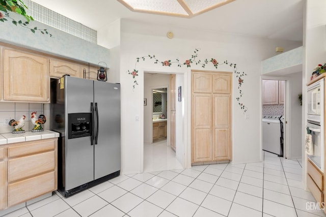 kitchen with tile countertops, light brown cabinets, white appliances, backsplash, and washer / clothes dryer