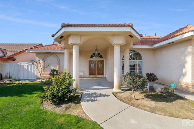 view of exterior entry with a tiled roof, a lawn, and stucco siding