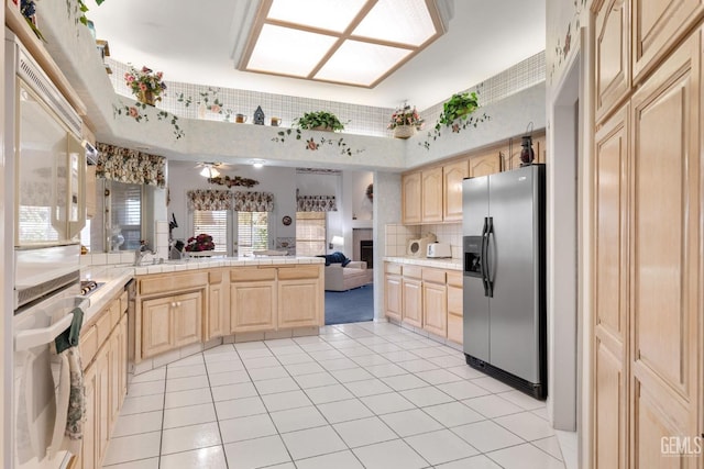 kitchen with a peninsula, light brown cabinets, stainless steel refrigerator with ice dispenser, and light countertops