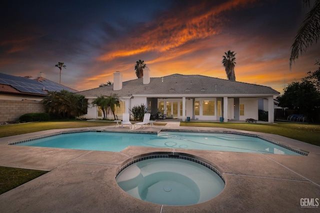 pool at dusk with an in ground hot tub, a patio area, and a lawn