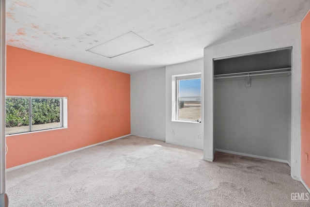 unfurnished bedroom with a closet, attic access, and carpet