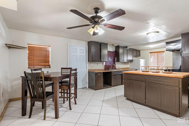 kitchen with freestanding refrigerator, light tile patterned floors, dark brown cabinetry, a ceiling fan, and a sink