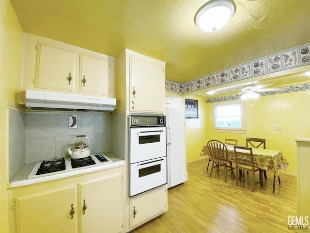 kitchen featuring white cabinetry, ceiling fan, backsplash, white appliances, and light wood-type flooring