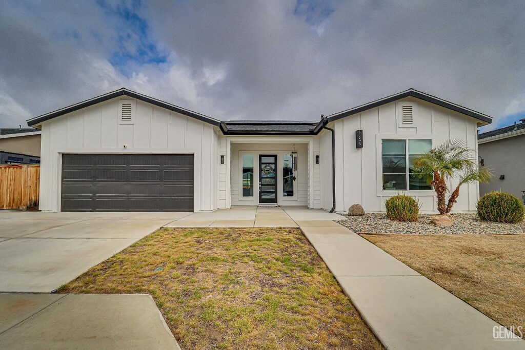 view of front facade featuring board and batten siding, concrete driveway, an attached garage, and fence