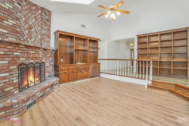 unfurnished living room featuring ceiling fan, light wood-style floors, visible vents, and a brick fireplace