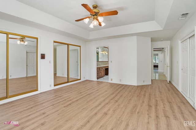 unfurnished bedroom featuring light wood finished floors, two closets, ensuite bath, visible vents, and baseboards