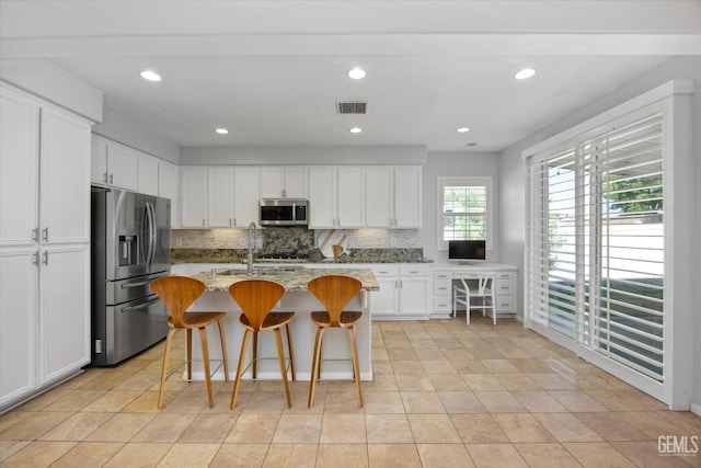10002 Riata Ln, Bakersfield, CA 93306 - kitchen with appliances with stainless steel finishes, decorative backsplash, white cabinets, a breakfast bar area, and a sink