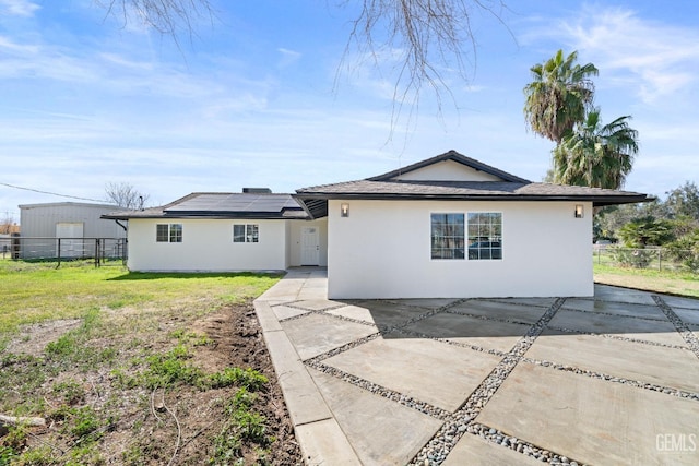 back of house featuring a yard, fence, solar panels, and stucco siding