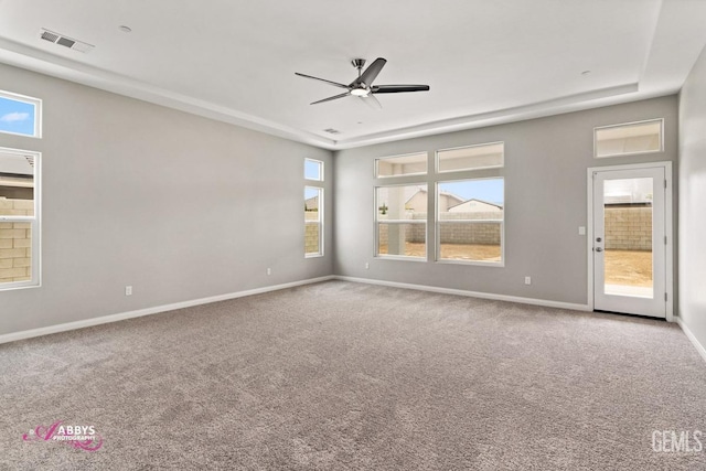 empty room with ceiling fan, a raised ceiling, and carpet floors