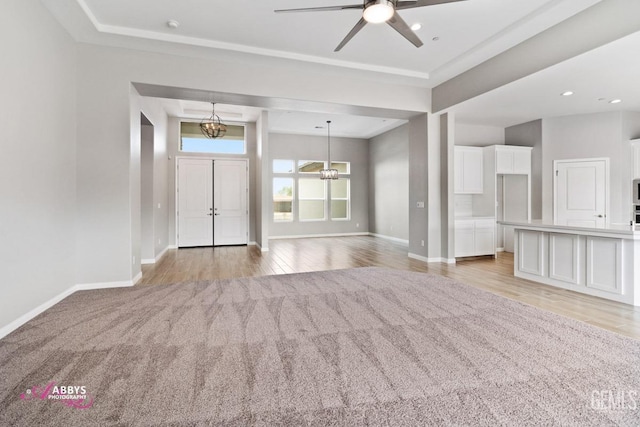 unfurnished living room featuring a raised ceiling, ceiling fan with notable chandelier, and light hardwood / wood-style flooring