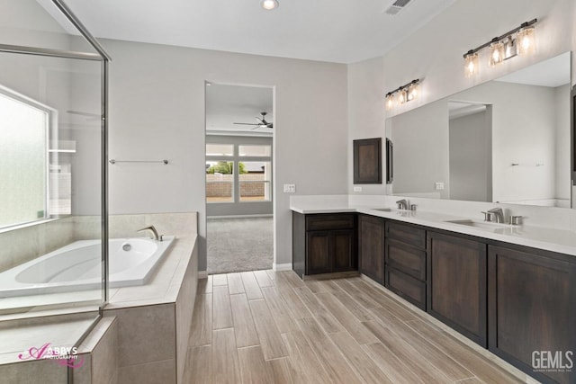 bathroom with ceiling fan, vanity, and tiled bath