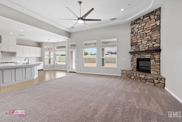 unfurnished living room with light colored carpet, sink, a stone fireplace, and ceiling fan with notable chandelier