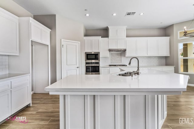 kitchen with built in microwave, sink, an island with sink, and stainless steel oven