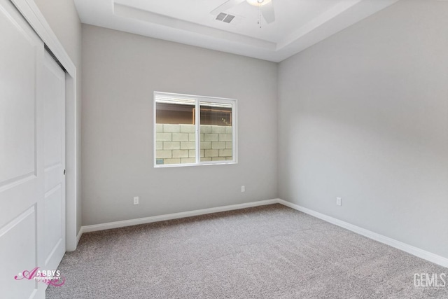 unfurnished bedroom with a closet, carpet floors, ceiling fan, and a tray ceiling