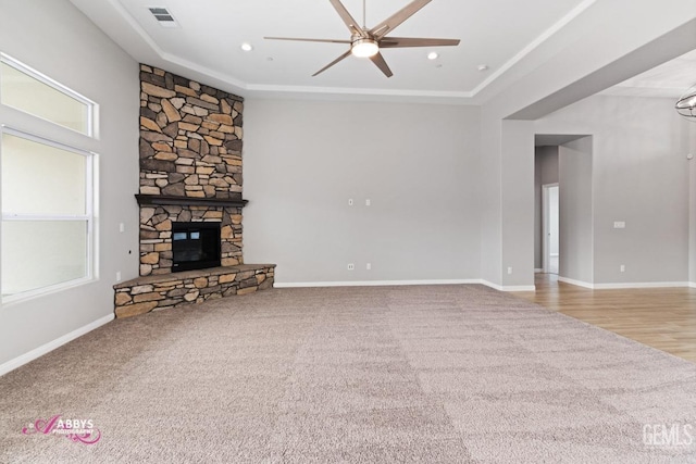 unfurnished living room with a raised ceiling, a stone fireplace, carpet flooring, and ceiling fan