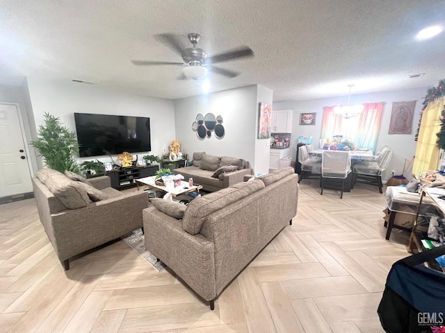 living room featuring a textured ceiling and ceiling fan with notable chandelier