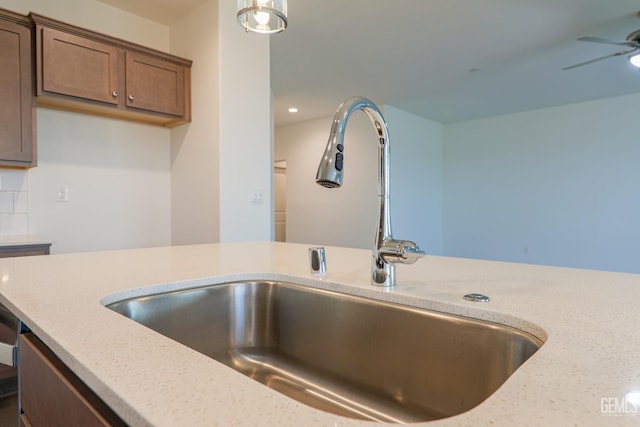 kitchen featuring light stone counters, ceiling fan, and sink