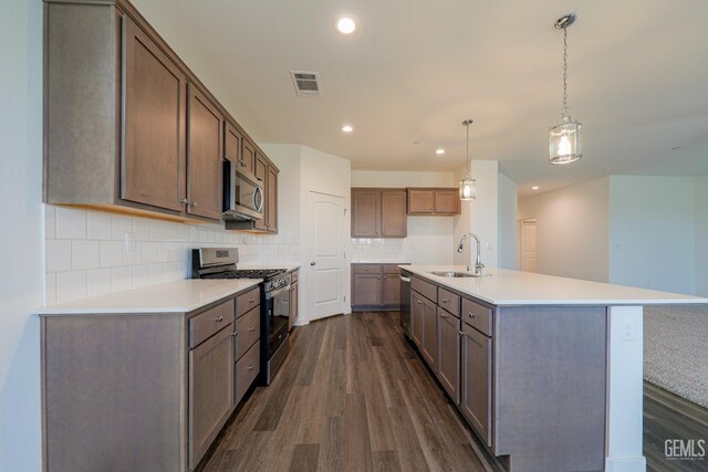 kitchen featuring sink, dark hardwood / wood-style floors, decorative light fixtures, a kitchen island with sink, and appliances with stainless steel finishes