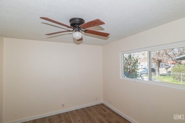 empty room with a textured ceiling, dark wood-style flooring, and baseboards