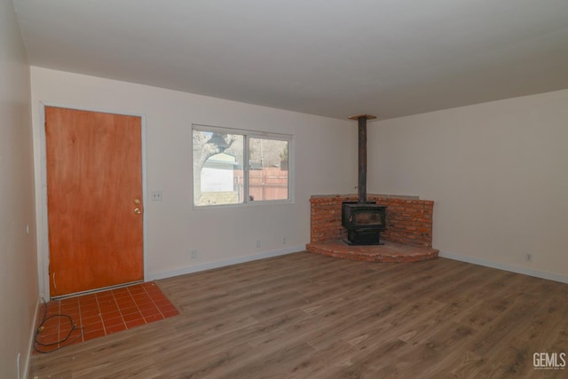 unfurnished living room with a wood stove, baseboards, and wood finished floors