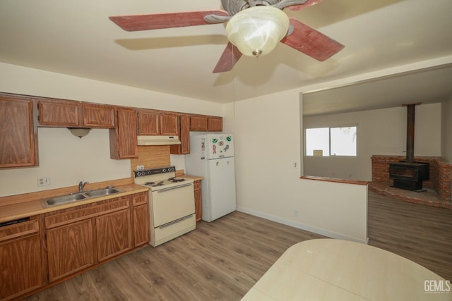 kitchen with under cabinet range hood, white appliances, a sink, light countertops, and brown cabinetry