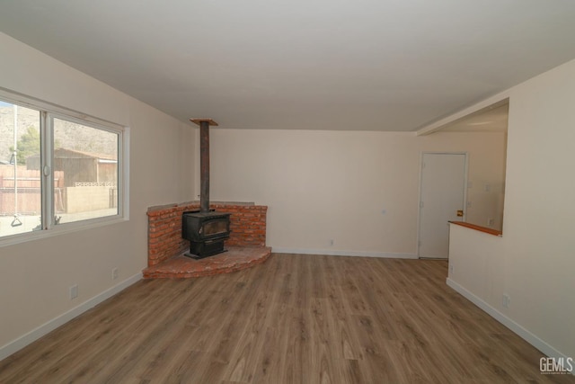 unfurnished living room featuring wood finished floors, a wood stove, and baseboards