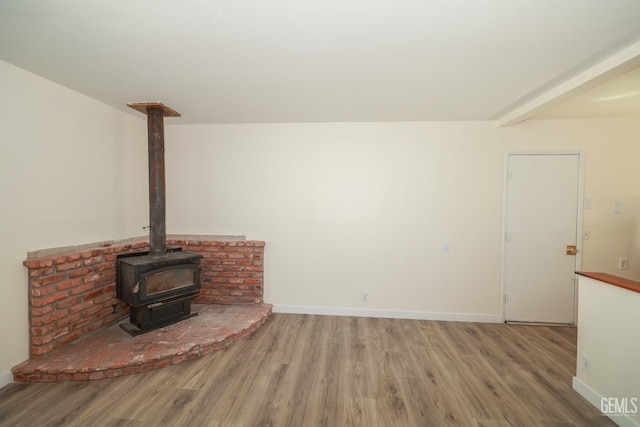 living room with beamed ceiling, wood finished floors, a wood stove, and baseboards