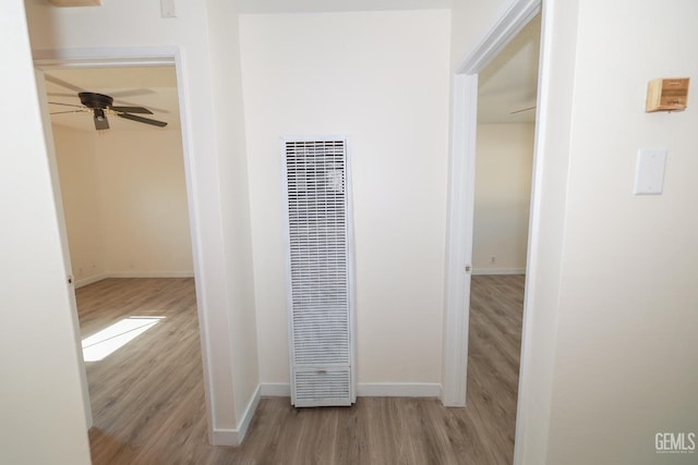 hallway with light wood finished floors, baseboards, and a heating unit